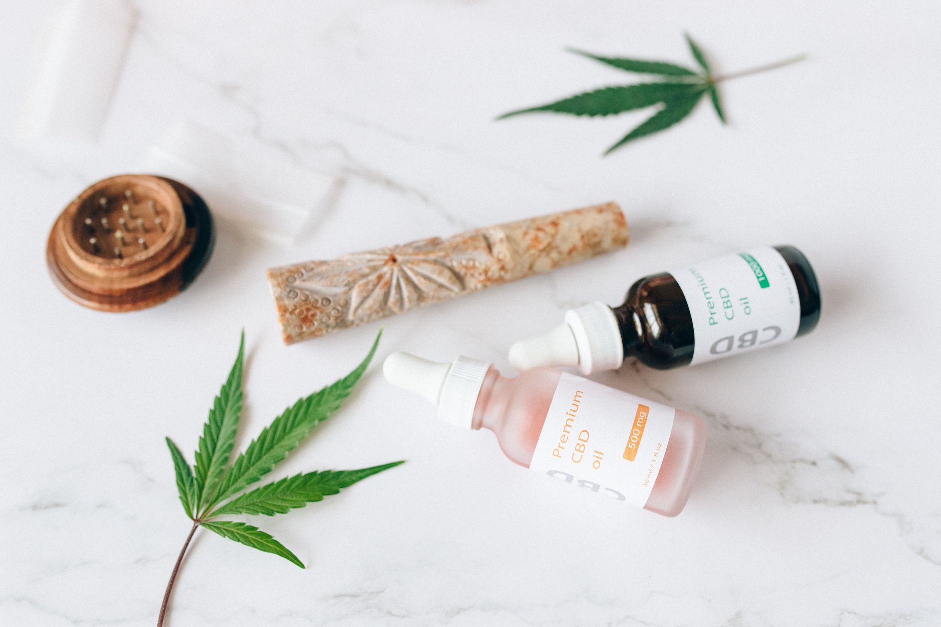 Composição de frascos de conta-gotas de óleo de CBD e folhas de cânhamo sobre uma superfície de mármore.